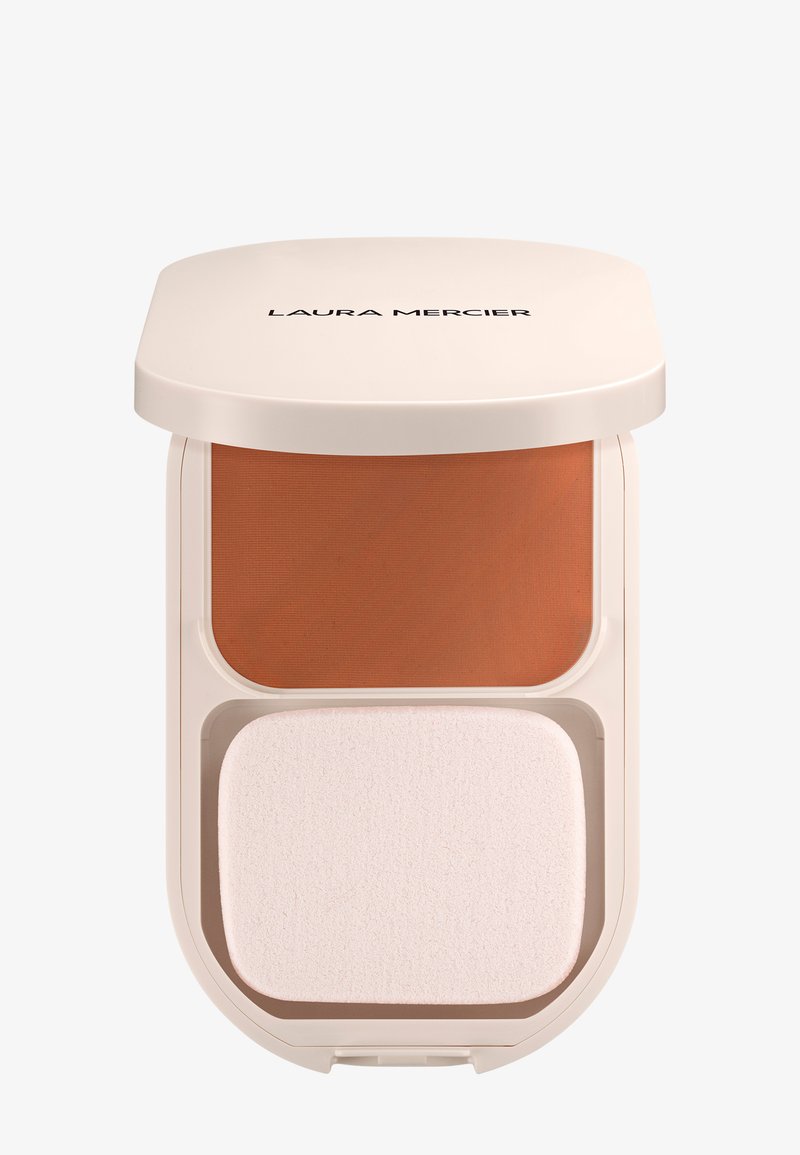 Estuche compacto beige etiquetado como Laura Mercier que contiene polvo de maquillaje naranja quemado y una esponja aplicadora blanca rectangular.