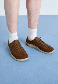 Braune Sneakers aus Wildleder und Leder, mit einer Gummisohle, runder Form und sechs Ösen mit passenden braunen Schnürsenkeln.