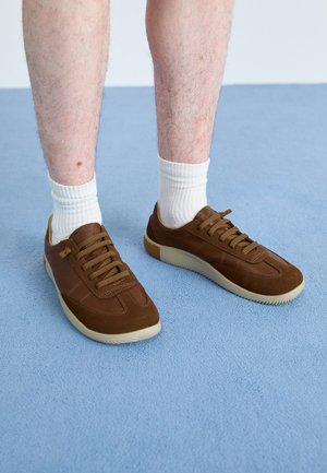 Baskets marron en daim et en cuir, dotées d'une semelle en caoutchouc, d'une forme arrondie et de six œillets avec des lacets marron assortis.