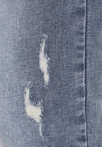 Jeans din denim de un albastru deschis, cu rupture desfăcute, textură moale și o vedere detaliată a țesăturii fabricii și a zonelor uzate.
