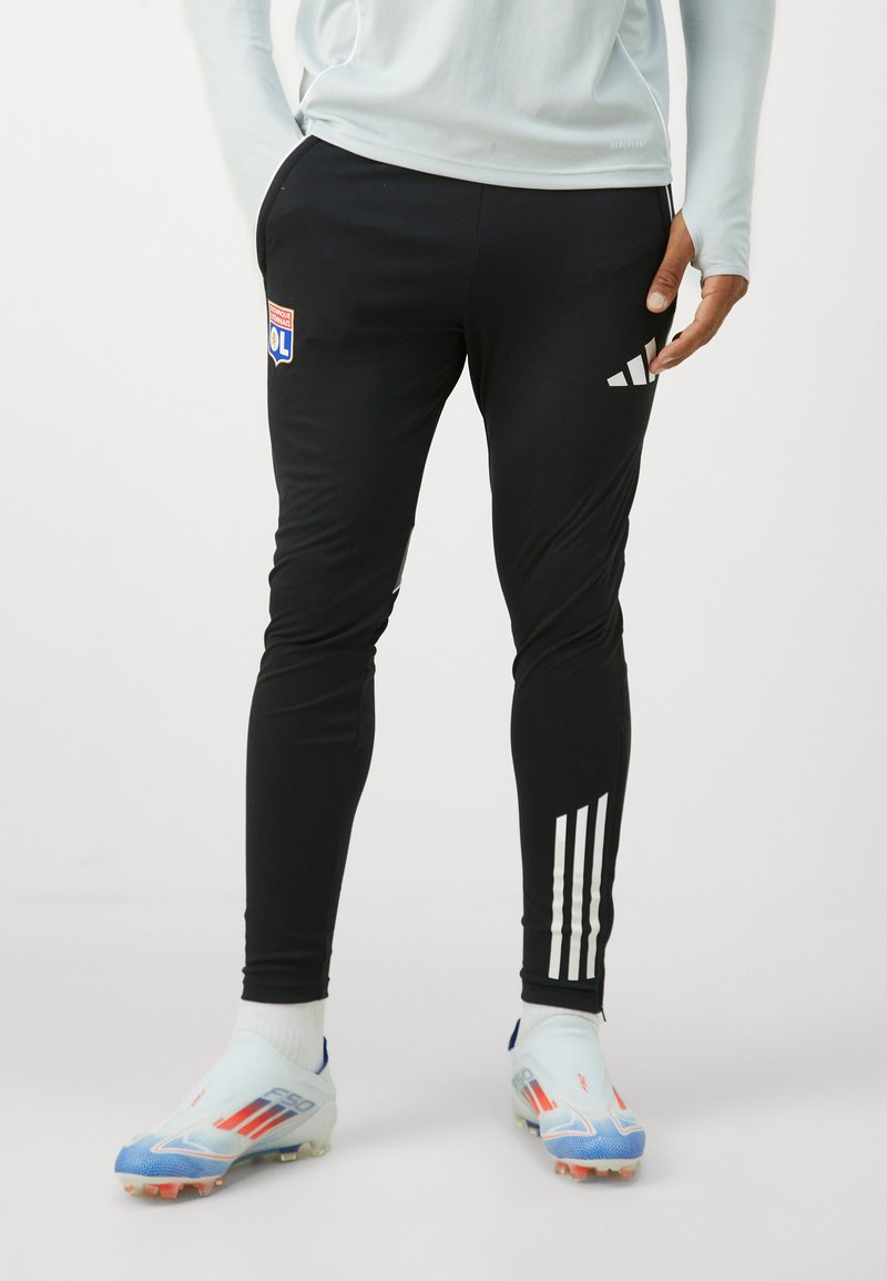 Pantalones deportivos negros con rayas blancas de Adidas, con un parche de logo en el muslo y un diseño ajustado, adecuados para actividades deportivas.