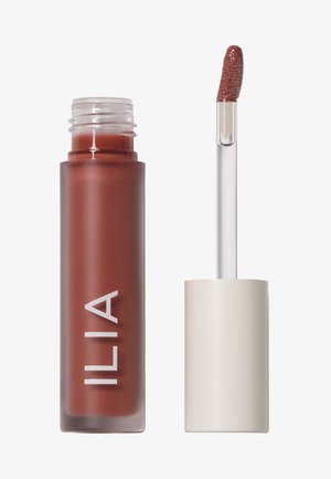 ILIA vloeibare lippenstift in een matte, diepe terracottakleur. Duidelijke applicator met een gestructureerde doe-foot tip. Strakke, cilindrische verpakking.
