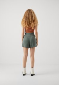 Zelené šortky s hladkým povrchem a elastickým pasem, spárované s vzorovaným crop topem. Bílé kotníkové boty doplňují celý outfit.