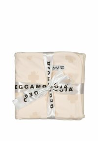 Beige filt med ett mjukt blommönster, knuten med ett satinband. Märkesetiketten "Geggamoja Collection" är synlig.