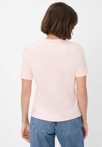 T-shirt rosa a maniche corte con scollatura rotonda e una texture liscia. La maglietta ha un orlo dritto ed è indossata con jeans blu.