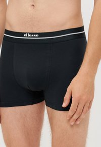 Fekete boxer alsónemű, kontrasztos elasztikus derékpánttal, melyen a "ellesse" márkaneve fehér színben található. Simább, rugalmas anyagból készült.