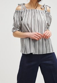 Randig avaxlat blus med korta puffärmar, rosettdetaljer på axelbanden, tillverkad av lätt tyg i vitt och svart.