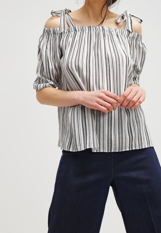 Randig avaxlat blus med korta puffärmar, rosettdetaljer på axelbanden, tillverkad av lätt tyg i vitt och svart.