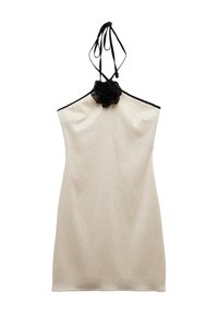 Beige halterneck mekko, jossa on musta reuna ja musta kangaskukka yksityiskohtana kauluksessa, valmistettu hieman kiiltävästä tekstuurikankaasta.
