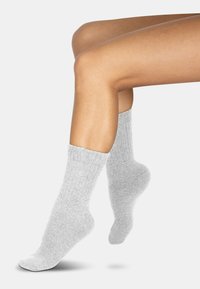 Graue Baumwoll-Short-Socken mit geripptem Bündchen und glatter Textur, die auf einem Bein vor weißem Hintergrund ruhen.