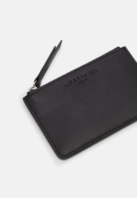 Czarny portfel ze skóry o fakturowanej powierzchni, z zamkiem błyskawicznym, małą zawieszką i wytłoczonym logo marki na przodzie.