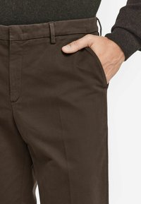 Bruna bomullsbukser med flat framsida, sidofickor och en slät yta. Midjan har bältesöglor.