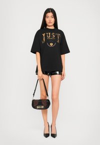 Black oversized t-shirt with metallic gold print, paired with shiny black shorts. Accessories include a textured black and brown bag.
