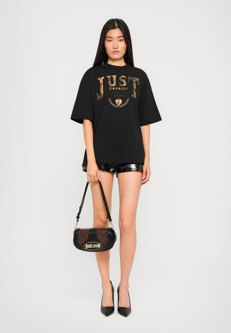 Black oversized t-shirt with metallic gold print, paired with shiny black shorts. Accessories include a textured black and brown bag.