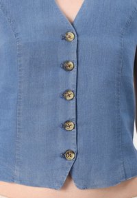 Denim jakna v svetlo modri barvi z V-izrezom in petimi bež gumbi spredaj. Tkanina je gladka z rahlo teksturiranim zaključkom.