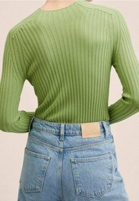 Personne portant un pull côtelé vert clair rentré dans un jean en denim bleu clair taille haute avec des poches arrière et une étiquette en cuir beige.