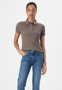 Karamellfarbener Poloshirt mit kurzen Ärmeln aus strukturiertem, geripptem Design, mit Kragen und drei Knopfverschluss, kombiniert mit blauen Jeans.