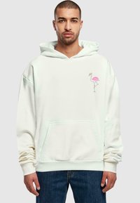 Hvid hoodie med kængurulomme, der har et grafisk tryk af en pink flamingo til venstre. Blødt stof og afslappet pasform.