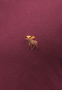 Bordowy sweter z dzianiny z haftowanym brązowym łosiem o żółtych rogach, umieszczonym po lewej stronie. Gładka faktura, casualowy styl.