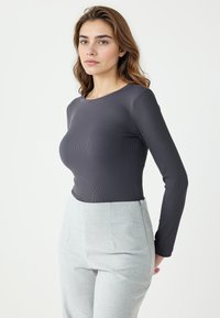 Dunkelgraues, geripptes Langarmoberteil mit rundem Halsausschnitt, kombiniert mit hellgrauen, maßgeschneiderten Hosen in glatter Textur und strukturierter Passform.