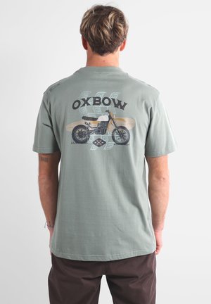 T-shirt en coton vert clair avec un graphisme de moto et le texte "OXBOW" en impression foncée au dos. Coupe décontractée avec des manches courtes.