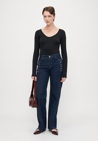 Μαύρο bodysuit με μακρύ μανίκι, ψηλόμεσα σκούρα τζιν παντελόνια με λεπτομέρειες καρώ στο πλάι, μπορντό τσάντα και παπούτσια με μυτερή μύτη.