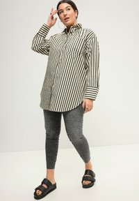 Pruhovaná košile s knoflíky v krémové a černé barvě, se kapsou, spárovaná se šedými skinny džíny a černými sandály na klínku s širokými popruhy.
