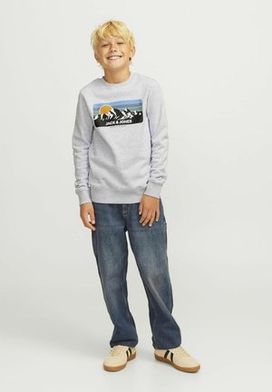 Sweatshirt gris avec un design graphique représentant des montagnes et un soleil. Associé à un jean en denim bleu et des baskets beiges avec des rayures noires.