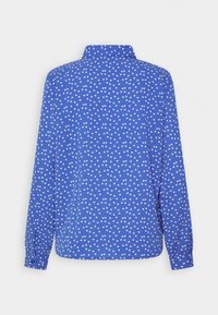 Chemise bleu à manches longues avec des pois blancs, dotée d'un col à revers et de poignets boutonnés. Tissu léger offrant une texture douce.