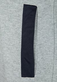 Szara bluza z kapturem z kontrastową czarną boczną kieszenią. Materiał wydaje się miękki i teksturowany, z widocznymi detalami szwów.