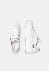 Baskets blanches avec des panneaux en mesh, des accents texturés gris, et un motif décoratif sur le talon. Elles disposent de fermetures à lacets et à zip.
