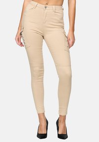 Pantalones cargo beige con un ajuste slim, que cuentan con bolsillos laterales y una textura suave. El diseño de cintura alta se combina con tacones altos negros para crear un contraste.