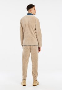 Sudadera de forro polar beige y pantalones a juego. Textura suave y esponjosa, corte relajado y puños elásticos. El cuello presenta un acento azul contrastante.