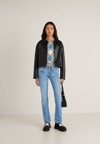 Orezaná čierna kožená bunda cez sivý argyle sveter, kombinovaná so svetlo modrými džínsami a čiernymi platformovými topánkami. V ruke čierna taška.