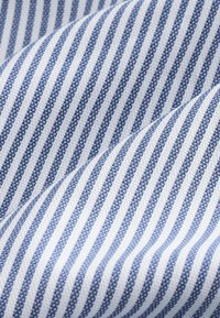 Tela a rayas azul y blanca, con líneas diagonales de diferentes anchos y un tejido texturizado. El patrón es consistente y presenta un acabado limpio.