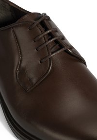 Braune Leder Schuhe mit einer glatten Oberfläche, traditionellem Schnürdesign, runder Zehenform und sichtbaren Nähten.