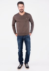Brown knitted sweater with V-neck, paired with dark blue denim jeans and black sneakers with white laces. Simple design, no patterns.