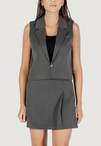 Gilet grigio su misura con colletto a revers e chiusura con un bottone, abbinato a una gonna plissettata coordinata, entrambi in un tessuto liscio.