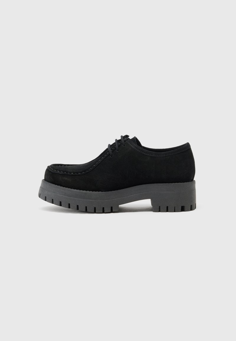 Chaussure en daim noir avec une semelle épaisse et robuste en caoutchouc gris. Dispose d'un bout arrondi et de lacets, avec une surface texturée et des détails de couture.