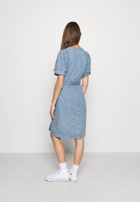Denim-asu, jossa on puffi hihat, vyötäröllä vyö, polvipituinen helma ja vaaleansininen väri. Yhdistetty valkoisiin lenkkareihin ja sukkiin.