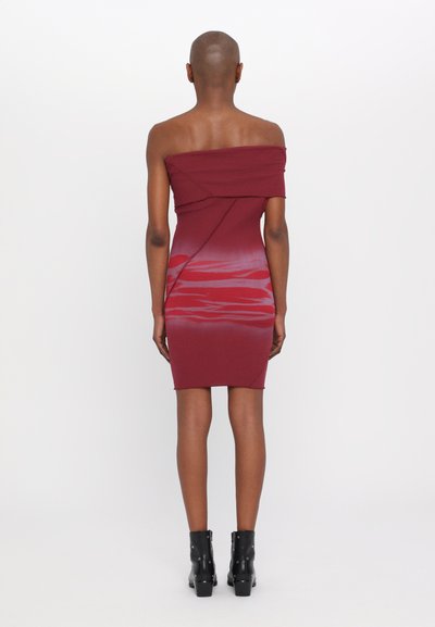 Abito bordeaux off-shoulder con silhouette aderente, caratterizzato da una sottile texture a gradiente e dettagli arricciati lungo la schiena. Stivaletti neri fino alla caviglia.