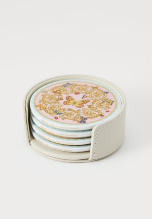 Zestaw czterech okrągłych ceramicznych podkładek z różowym kwiatowym wzorem, złotymi akcentami i beżowym stojakiem, pełniących funkcję dekoracyjną.