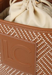 Bolso de cuero marrón tejido con un interior de tela beige claro. Incluye un distintivo logotipo en relieve "LC" en un parche de cuero suave.
