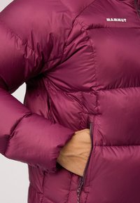 Bordowy puchowy kurtka z pikowanym wzorem, z zamkiem błyskawicznym w kieszeni i gładką, błyszczącą teksturą. Logo nadrukowane na obszarze klatki piersiowej.