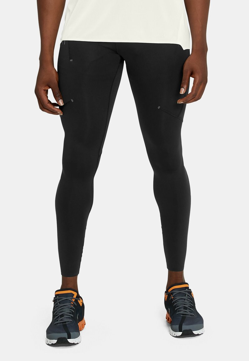 Sorte atletiske leggings med en tætsiddende design, der har sidelommer og diskret søm detaljer, parret med mørke atletiske sko.