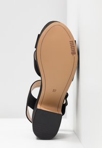 Sandale noire à talon bloc vue de la semelle, taille 37 avec la marque "mtng" sur la semelle couleur tan sur fond blanc.