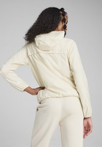 Ljusbeige huva jacka med en figurnära design, elastiska manschetter och en slät, matt yta. Bärs över matchande byxor.