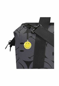 Borsa nera con finitura lucida, caratterizzata da un motivo astratto grigio, manici robusti e un ciondolo a forma di faccina sorridente gialla attaccato alla cerniera.