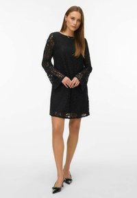 Mustast pitskleidist pikkade kellukeste varrukatega, millel on lillemustriga sirge lõige. Kanditud mustade teravate kontsadega kingadega.