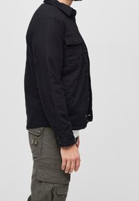 Svart bomulljacka med knäppning fram, krage och fickor med lappar. Buren tillsammans med olivgröna cargobyxor med sidfickor.